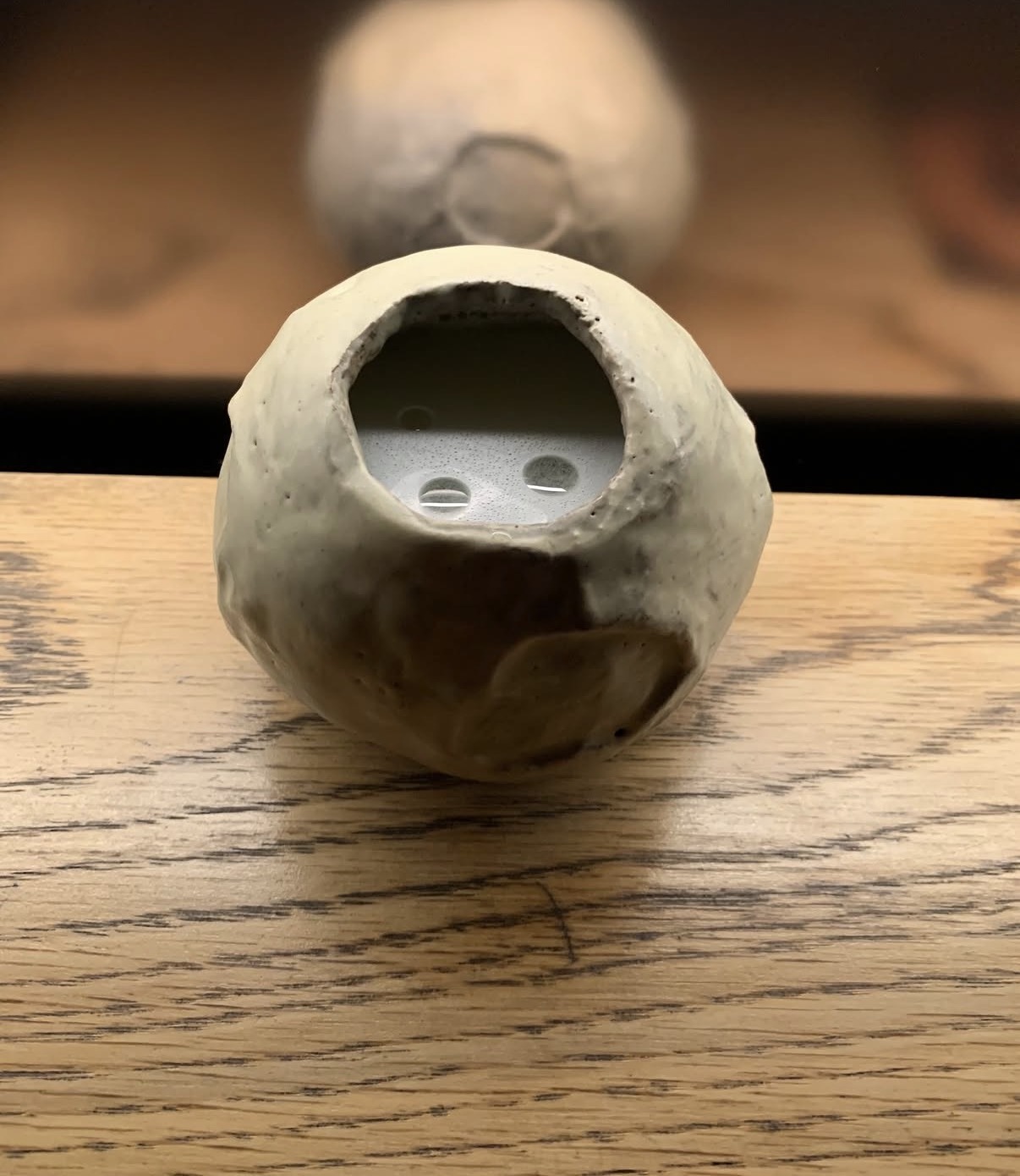 Clear drink served in a hand-sculpted ceramic vessel on a wooden bar
